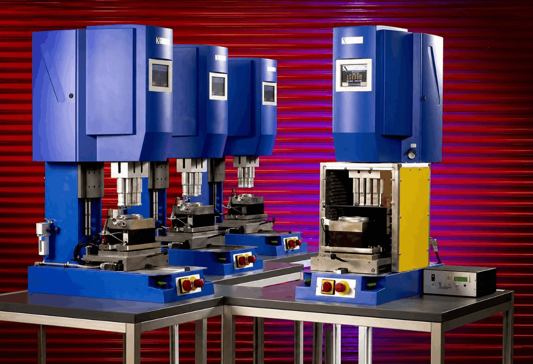 Industrial ultrasonic welding setup featuring multiple blue press units aligned on a workbench, illustrating precision tooling used in ultrasonic welding systems, including sonotrodes, boosters, and horns, against a high-contrast red and purple background.